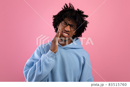 Unhappy black teenager suffering from tooth ache, having gum problems, touching his cheek on pink studio background Unhappy black teenager suffering from tooth ache, having gum problems, touching his cheek on pink studio background 83515760