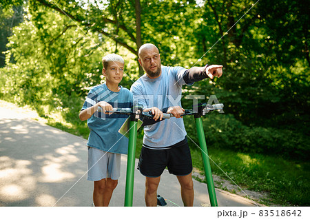 Father and son riding on kick scooters in park Father and son riding on kick scooters in park 83518642