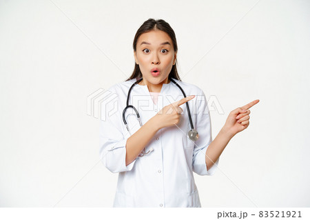 Surprised female doctor say wow, pointing right and looking amazed with discounts in clinic, showing way, standing in medical uniform against white background 83521921