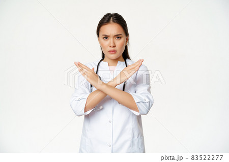 Serious asian woman doctor prohibit patient behaviour, showing stop, cross arms gesture, frownign displeased, disapprove smth bad, standing over white background 83522277