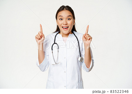Excited smiling nurse, female doctor in medical uniform pointing up, showing promo sale, healthcare clinic discount, standing over white background Excited smiling nurse, female doctor in medical uniform pointing up, showing promo sale, healthcare clinic discount, standing over white background 83522346
