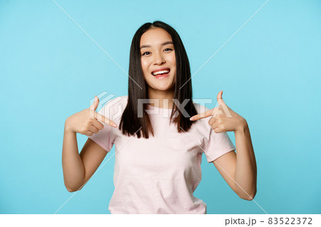 Confident korean woman smiling, makes smug face and points at herself, self-promoting, volunteering, being a winner, standing over blue background Confident korean woman smiling, makes smug face and points at herself, self-promoting, volunteering, being a winner, standing over blue background 83522372