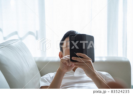 ソファに横になりスマホをいじる男性の様子 ソファに横になりスマホをいじる男性の様子 83524235