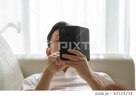 ソファに横になりスマホをいじる男性の様子 ソファに横になりスマホをいじる男性の様子 83524238