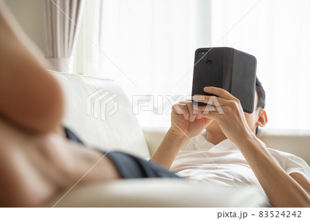 ソファに横になりスマホをいじる男性の様子 83524242