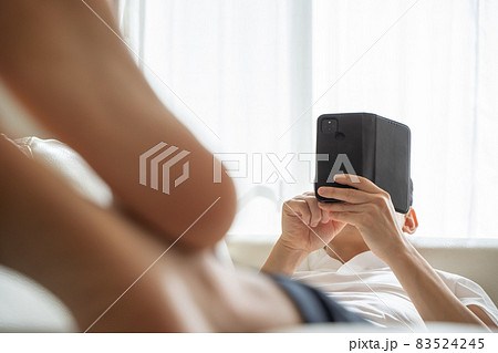 ソファに横になりスマホをいじる男性の様子 83524245
