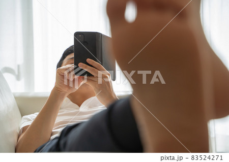 ソファに横になりスマホをいじる男性の様子 83524271