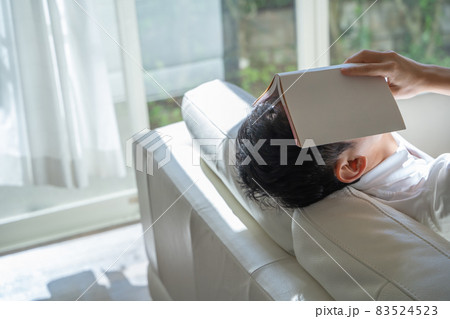 ソファに横になり本を顔にかぶせる男性の様子 83524523
