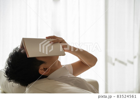 ソファに横になり本を顔にかぶせる男性の様子 83524561