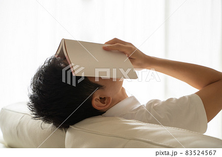 ソファに横になり本を顔にかぶせる男性の様子 83524567