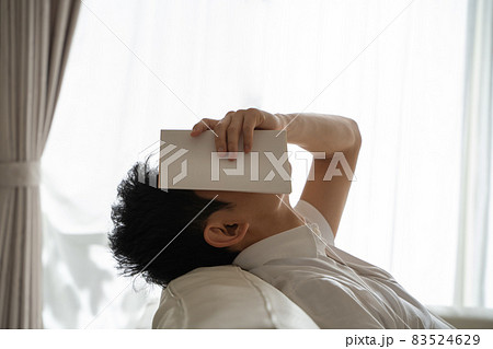 ソファに横になり本を顔にかぶせる男性の様子 ソファに横になり本を顔にかぶせる男性の様子 83524629