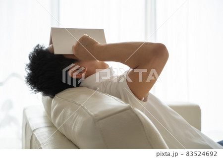 ソファに横になり本を顔にかぶせる男性の様子 ソファに横になり本を顔にかぶせる男性の様子 83524692
