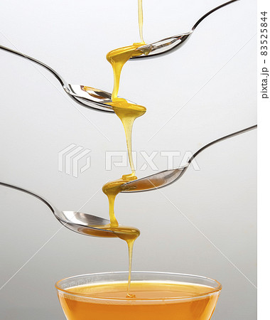 Fresh flower honey drips from a spoon into a spoon on a light background. Organic vitamin food. 83525844