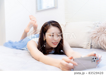 ベッドでうつ伏せでスマホの動画を見る女性 83529420