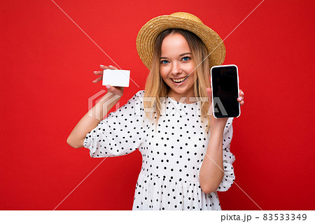 Shot of beautiful happy smiling blonde woman in summer clothes showing smartphone with empty screen Shot of beautiful happy smiling blonde woman in summer clothes showing smartphone with empty screen 83533349