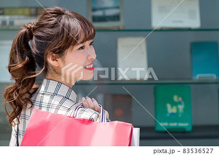 ショーウィンドーの前で紙袋を持って佇むショッピング中の若い女性 ショーウィンドーの前で紙袋を持って佇むショッピング中の若い女性 83536527