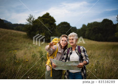 Happy mid adult woman with active senior mother hiking and looking at map outdoors in nature. 83538289