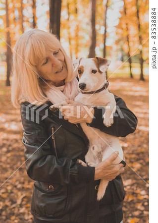 Senior smiling woman hugging her dog in autumn park. Active aging and pet concept. 83538884