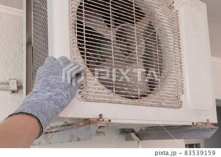 The hand of an air conditioner repair and maintenance specialist in a construction glove working with air-conditioned old equipment 83539159