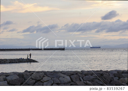 夕暮れ時の静かな海。親子3人釣りを楽しむシルエット。沖を汽船がゆく。 夕暮れ時の静かな海。親子3人釣りを楽しむシルエット。沖を汽船がゆく。 83539267