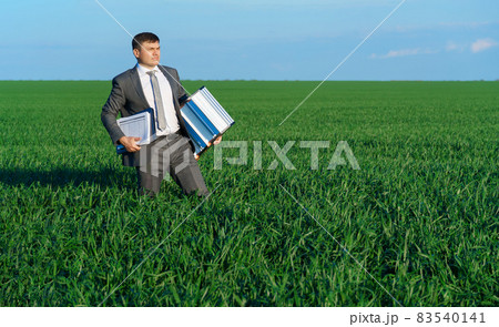 businessman poses in a green field, he goes with the documents and ladder, freelance and business concept, green grass and blue sky as background 83540141