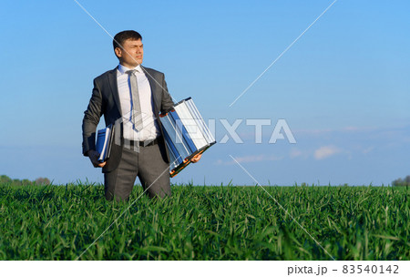 businessman poses in a green field, he goes with the documents and ladder, freelance and business concept, green grass and blue sky as background 83540142