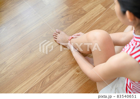 Asian woman sitting on the wooden floor hand holds her ankle injury. painful point. Health care and medical concept. 83540651