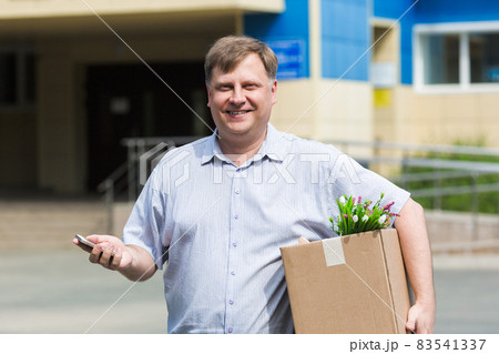 An adult man with a box of personal belongings calls on the phone about getting a new job An adult man with a box of personal belongings calls on the phone about getting a new job 83541337