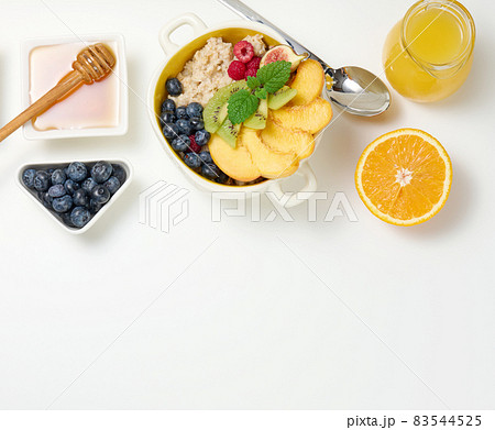 plate with oatmeal and fruit, half a ripe orange and freshly squeezed juice in a transparent glass decanter, honey in a bowl on a white table. Healthy breakfast plate with oatmeal and fruit, half a ripe orange and freshly squeezed juice in a transparent glass decanter, honey in a bowl on a white table. Healthy breakfast 83544525