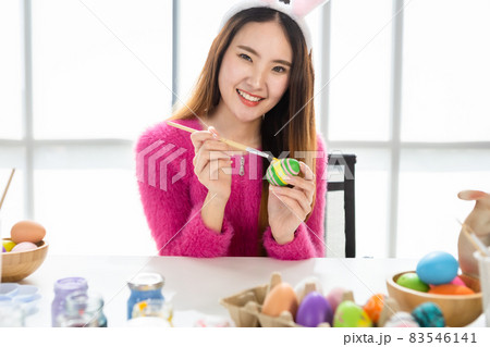 Easter holiday concept, Happy Asian Young woman wearing bunny ears hand painted eggs for Easter with colorful Easter eggs In the white room background 83546141