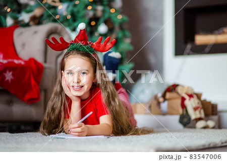 Funny cute caucasian girl left-handed writes a letter to Santa Claus near the Christmas tree. Happy childhood, time of miracles and desires. Funny cute caucasian girl left-handed writes a letter to Santa Claus near the Christmas tree. Happy childhood, time of miracles and desires. 83547006
