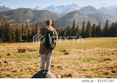 Young man in sunglasses with backpack see view on top mountain. Freedom, happiness, travel and vacations concept, outdoor activities. Man standing backwards looking away Young man in sunglasses with backpack see view on top mountain. Freedom, happiness, travel and vacations concept, outdoor activities. Man standing backwards looking away 83547295