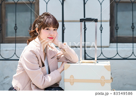 キャリーバックの前で座っている旅先の若い女性 83549586