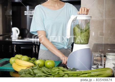 Close-up of unrecognizable woman standing at kitchen counter with kitchen counter and making green smoothie into blender Close-up of unrecognizable woman standing at kitchen counter with kitchen counter and making green smoothie into blender 83549874