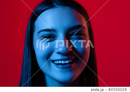 Close-up portrait of young beautiful woman smiling, posing isolated over red background in neon lights 83550329