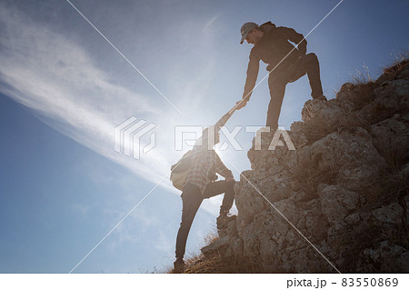 Silhouettes of two people climbing mountains and helping against the blue sky. Silhouettes of two people climbing mountains and helping against the blue sky. 83550869
