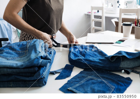 Denim Upcycling Ideas, Using Old Jeans, Repurposing Jeans, Reusing Old Jeans, Upcycle Stuff. Woman seamstress cut and repair old blue jeans in sewing studio. Denim Upcycling Ideas, Using Old Jeans, Repurposing Jeans, Reusing Old Jeans, Upcycle Stuff. Woman seamstress cut and repair old blue jeans in sewing studio. 83550950
