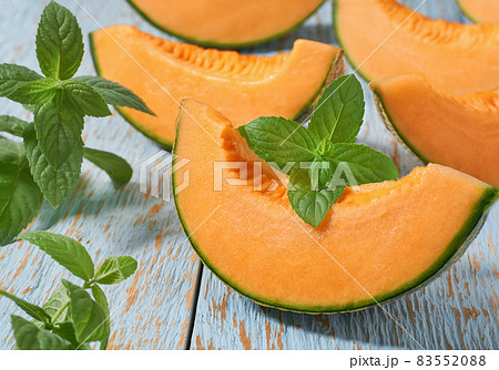 Sliced ripe cantaloupe melon and fresh mint on a wooden table. Sliced ripe cantaloupe melon and fresh mint on a wooden table. 83552088