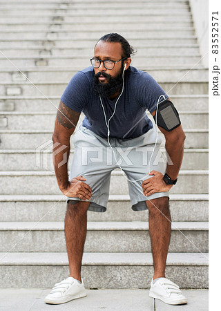 Exhausted young Indian man with beard leaning hands on knees while resting after running on stairs Exhausted young Indian man with beard leaning hands on knees while resting after running on stairs 83552571