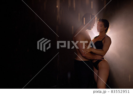 Temptive sensual couple posing in dark studio room, light and rain in the background 83552951