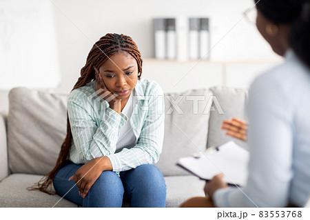 Sad black lady receiving psychological help at mental clinic, communicating with counselor 83553768
