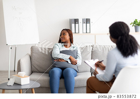 Black woman with nervous breakdown having session with psychologist, sitting on couch, hugging pillow at clinic Black woman with nervous breakdown having session with psychologist, sitting on couch, hugging pillow at clinic 83553872