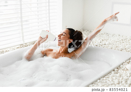 Pretty young woman taking bath with foam, using shampoo bottle as microphone, singing favorite song at home Pretty young woman taking bath with foam, using shampoo bottle as microphone, singing favorite song at home 83554021
