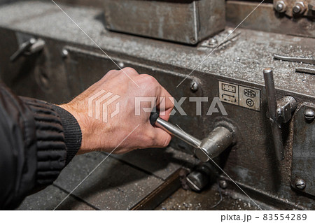 The hand of a man in a black work jumpsuit controls a milling machine by the handle for processing metal in an industrial enterprise The hand of a man in a black work jumpsuit controls a milling machine by the handle for processing metal in an industrial enterprise 83554289