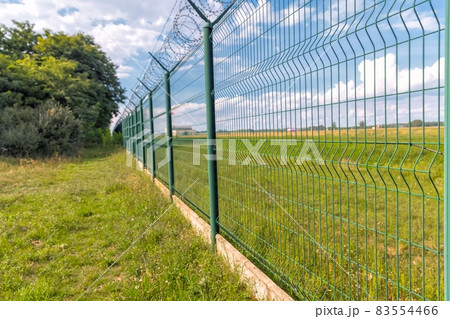 Tall fence with barbed wire angle shot Tall fence with barbed wire angle shot 83554466