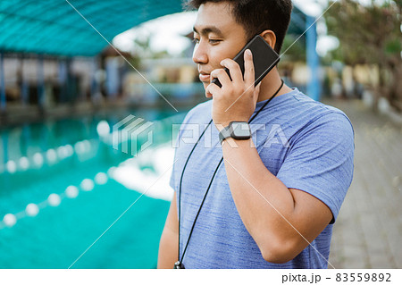a swimming coach wearing a stopwatch makes a phone call using a mobile phone a swimming coach wearing a stopwatch makes a phone call using a mobile phone 83559892