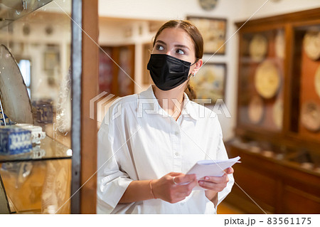 Portrait of female visitor in protective face mask with paper guide at paintings exposition 83561175