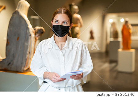 Positive female in protective mask with paper guide exploring sculpture art pieces in gallery Positive female in protective mask with paper guide exploring sculpture art pieces in gallery 83561246
