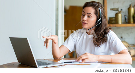 Smiling woman working at home in front of a laptop monitor. She held up her finger to indicate the importance of the idea. Format photo 2x1. 83561843