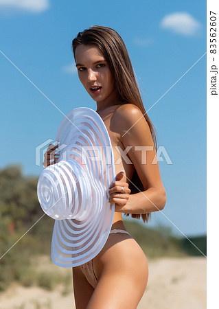 Sexy woman covering breast with sunhat on seashore 83562607